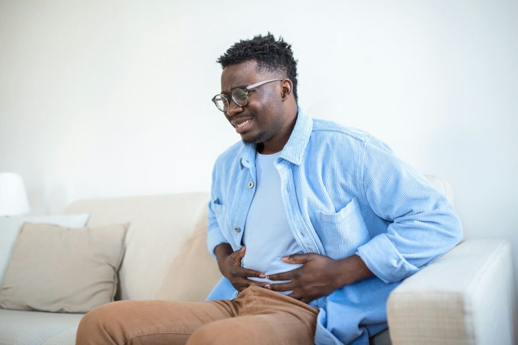 A Man Sitting On A Couch Holding His Stomach