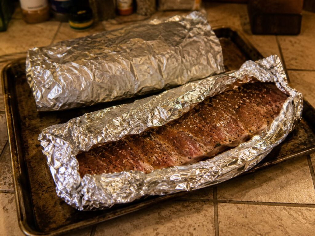 Seasoned Pork Spare Ribs Wrapped In Foil On A Baking Sheet Before Oven Cooking.